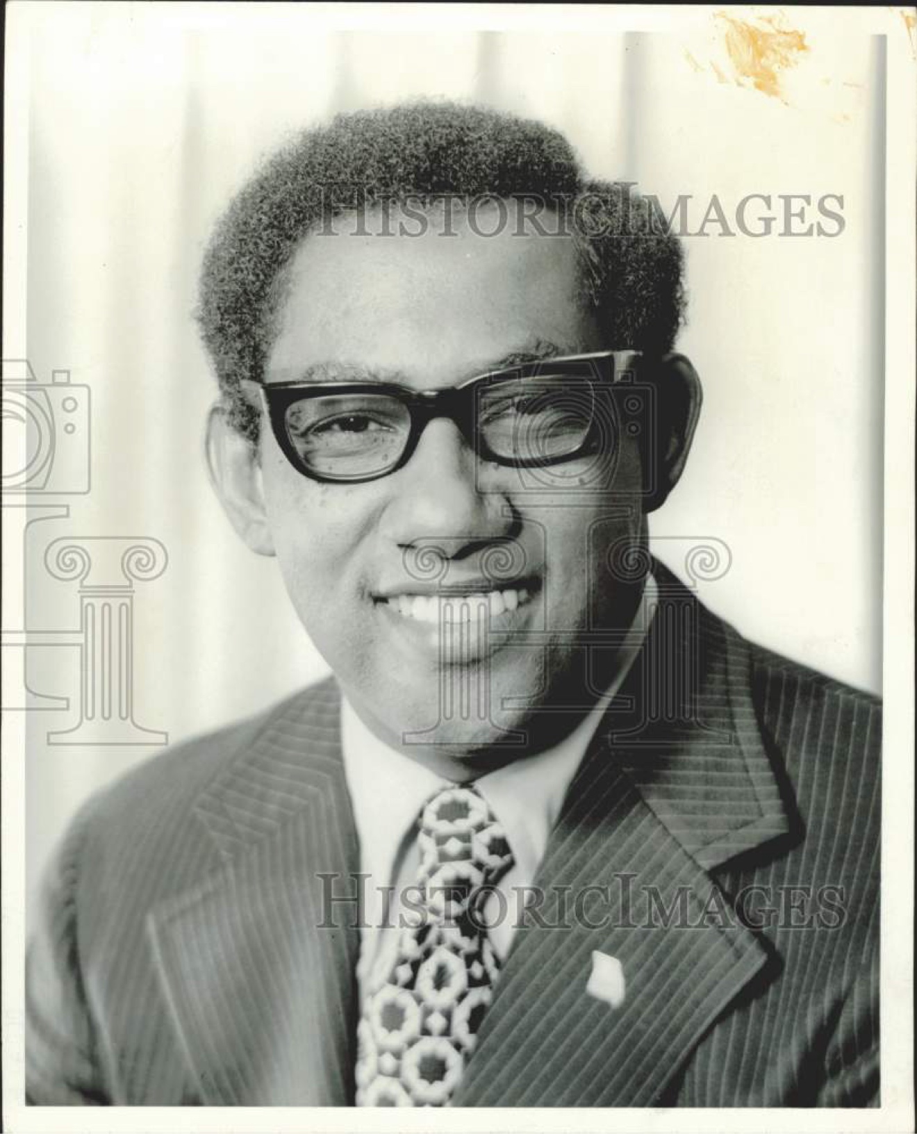 Dr. Samuel J. Cornelius — press portrait: smiling, in a pinstripe suit and patterned tie, wearing heavy-framed glasses